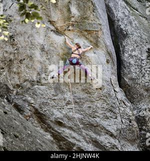 Junge Frau klettert schwierige Route auf einem hohen Felsen mit Seil. Furchtlose Kletterer trainieren am Sommertag Klettern. Konzept für Extremsport, Abenteuer und aktiven Lebensstil. Stockfoto