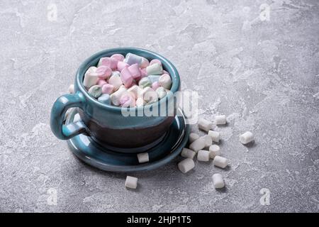 Große blaue Tasse mit Mini-farbigen Marschmalchen für heiße Schokolade, Kakao, lustige Party auf grauem Beton Hintergrund Stockfoto