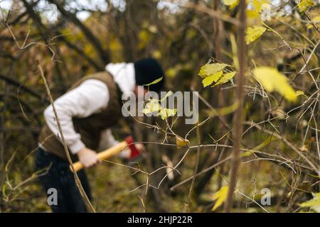 Tourist männlich trägt warme Kleidung Hacken Brennholz mit Axt im Wald an bewölkten kalten Tag, selektive Fokus. Stockfoto