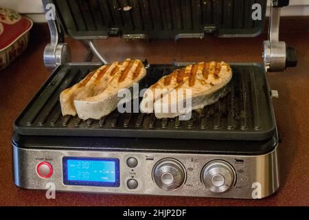 Moskau, Russland, November 2020: Heim tragbaren Grill in der Küche mit Lachsstücken, die auf einer heißen Oberfläche gebraten wird. Stockfoto