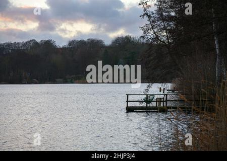 Holzdock mit Stuhl als Silhouette am Ufer eines Sees bei grauem, dunklem Wetter, idyllische Landschaft in unangenehmer Jahreszeit, Kopierraum, ausgewählt f Stockfoto