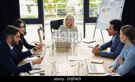 Eine Geschäftsfrau mittleren Alters, die bei einem Treffen mit multiethnischen Geschäftspartnern einen Laptop verwendet Stockfoto