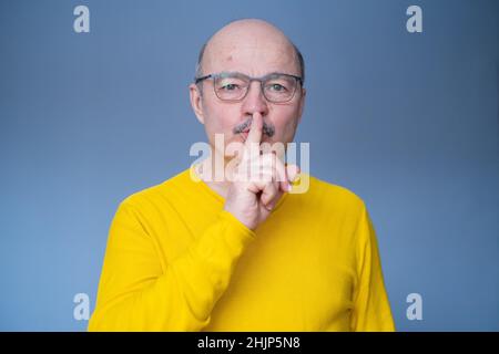 Ein älterer hispanischer Mann in einer Brille, der auf gelbem Hintergrund eine stille Geste machte Stockfoto