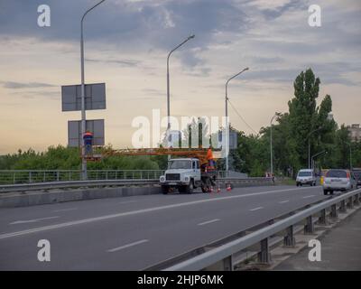 Auf Lastwagen montierte, hochfahrende Arbeitsbühne mit zwei Arbeitern, die ihre Arbeit am Abend auf einer Straßenbrücke in der Hauptstadt Kiew verrichten. Stockfoto