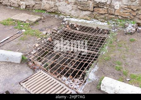 Altes rostiges Sturmgitter. Ein zerbrochener Sturmwasserkanal am Straßenrand in Feodosia Stockfoto