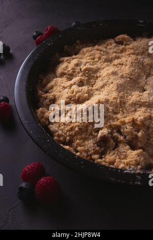 Hausgemachter Apfelbrösel mit Beeren bei schwachem Licht. Dunkles Food-Foto mit Kopierplatz. Stockfoto