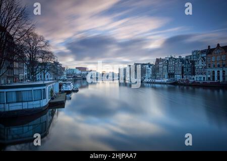 Blick auf den Amsterdamer Kanal bei Sonnenaufgang mit langer Belichtung, Hausboote und festfahrbare Flusskähne Amsterdam, Holland Stockfoto