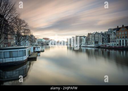 Blick auf den Amsterdamer Kanal bei Sonnenaufgang mit langer Belichtung, Hausboote und festfahrbare Flusskähne Amsterdam, Holland Stockfoto