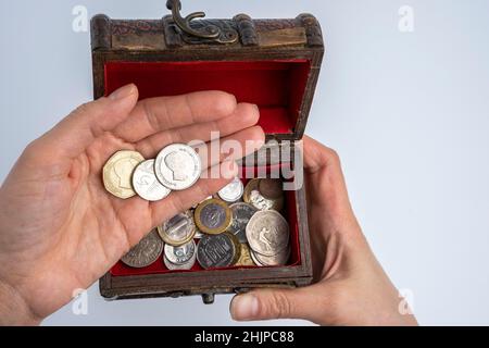 Eine kleine alte Holzkiste und weibliche Hände zählen Münzen auf weißem Hintergrund. Ersparnisse und Inflation Stockfoto