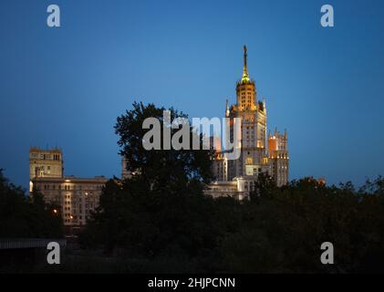 Das Hochhaus am Kotelnicheskaya-Ufer des Moskwa-Flusses heißt Stalin-Wolkenkratzer. Mit Stadtlichtern. Am Abend blauer Himmel. Stockfoto