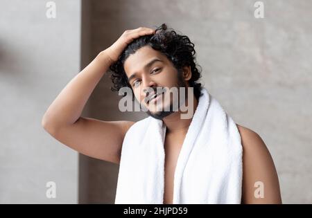 Männliche Morgenroutine. Hübscher indischer Mann mit Handtuch auf der Schulter im Badezimmer stehend, Platz kopieren Stockfoto