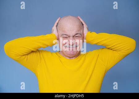 Ein verläßter älterer Mann, der seine Ohren mit erhobenen Handflächen bedeckte und schreckliche Kopfschmerzen hatte. Studioaufnahme. Geräuschkulisse um das Konzept herum. Stockfoto