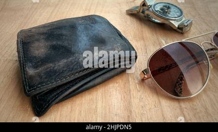 Alte Brieftasche auf dem Holztisch mit Uhr und alter Sonnenbrille im Hintergrund. Konzeptionell Stockfoto