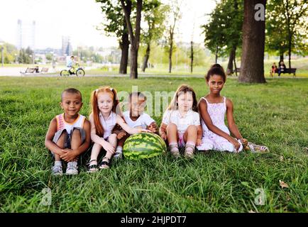 Vorschulkinder im Park auf dem Gras mit einer riesigen Wassermelone Stockfoto