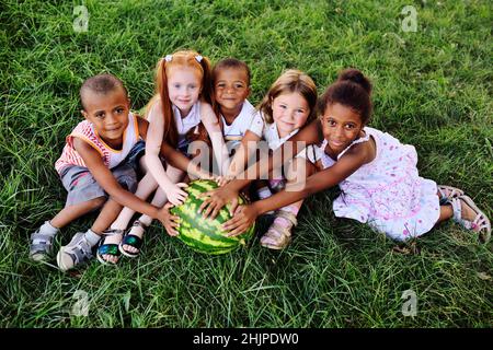 Vorschulkinder im Park auf dem Gras mit einer riesigen Wassermelone Stockfoto