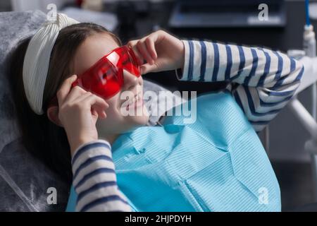 Das kleine Mädchen sitzt in einem Zahnarztstuhl und trägt eine Schutzbrille. Sie dubelt Stockfoto