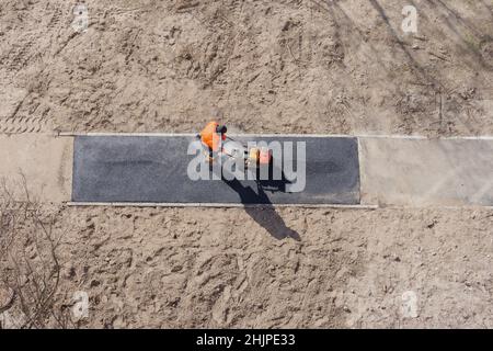 Neuer Asphaltbauarbeiter, der Straßenbelag auf Gehweg legt, auf Asphalt. Gehweg Bau Straße Bodenarbeit Asphalt. Bodenarbeiten Asphalt Pflaster Stockfoto