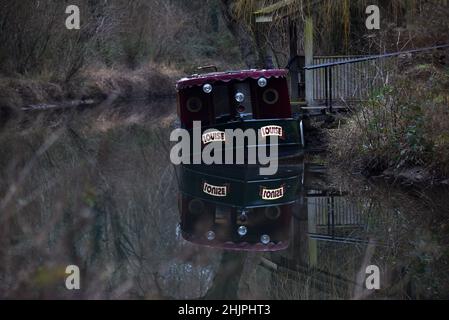 Ein Boot spiegelt sich im perfekt ruhigen Wasser des schönen Basingstoke Canal in der Nähe von Odiham wider Stockfoto