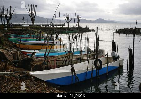 Traditionelle kleine Fischerboote vertäuten an einem launischen Tag in einem kleinen Hafen in San Feliciano am Trasimeno See. Hügel im Hintergrund Stockfoto