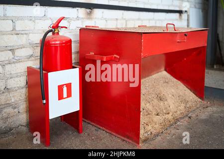 Primäre Löschmittel im Brandfall oder bei Entzündung, Feuerlöscher und eine Feuerlöschbox mit Sand im Produktionsraum des Industrieunternehmens. Stockfoto