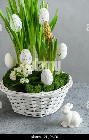 Blumenarrangement im Osterfrühling mit gelben Narzissen und weißen Eiern im Blumentopf auf einem grauen Tisch. Festliche vertikale Grußkarte. Stockfoto