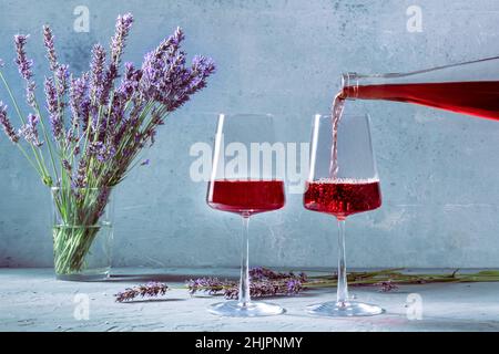 Wein aus einer Flasche in Gläser gegossen, mit Lavendelblüten im Hintergrund. Eine Verkostung provenzalischer Weine Stockfoto