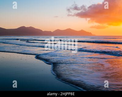 Küstenlinie am leeren Strand bei Ebbe mit Llyn Peninsula in Silhouette bei Sonnenuntergang. Dinas Dinlle, Gwynedd, Nordwales, Großbritannien Stockfoto