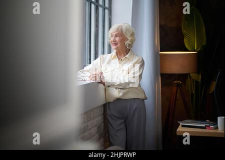 Frau, die neben dem Fenster steht und lächelt meditiert Stockfoto