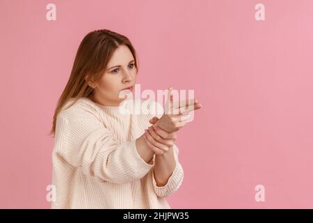 Porträt einer blonden Frau, die mit dem Fingergewehr auf die Kamera zeigt, mit Pistolenhandgeste anvisieren und drohen, mit weißem Pullover zu schießen. Innenaufnahme des Studios isoliert auf rosa Hintergrund. Stockfoto