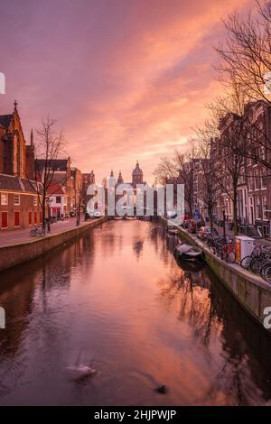 St. Nicolas Kirche und Brücke mit Blick auf einen Amsterdamer Kanal bei Sonnenaufgang mit Kanalbooten und Fahrrädern Amsterdam Holland Stockfoto