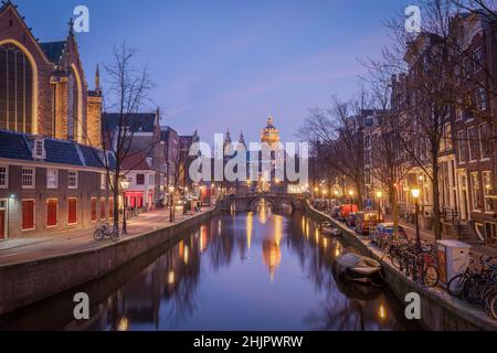 St. Nicolas Kirche und Brücke mit Blick auf einen Amsterdamer Kanal bei Sonnenaufgang mit Kanalbooten und Fahrrädern Amsterdam Holland Stockfoto