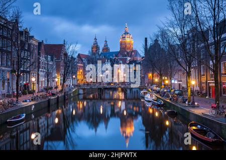 St. Nicolas Kirche und Brücke mit Blick auf einen Amsterdamer Kanal bei Sonnenaufgang mit Kanalbooten und Fahrrädern Amsterdam Holland Stockfoto