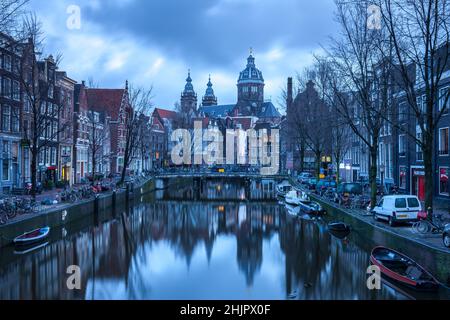 St. Nicolas Kirche und Brücke mit Blick auf einen Amsterdamer Kanal bei Sonnenaufgang mit Kanalbooten und Fahrrädern Amsterdam Holland Stockfoto