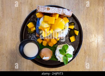 Mango-Eis serviert mit thailändischem klebrigen Reis auf einem Holzboden. Stockfoto