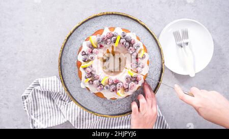 Flach liegend. Schritt für Schritt. Schneiden von Zitrone Cranberry Bundt Kuchen mit Zucker Cranberries und Zitronenkeile verziert. Stockfoto