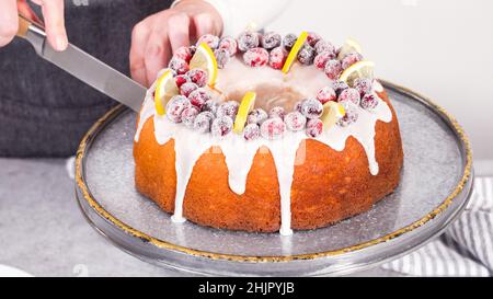 Schritt für Schritt. Schneiden Sie den mit Zuckercranberries und Zitronenkeilchen dekorierten Zitronenkuchen mit Preiselbeeren. Stockfoto