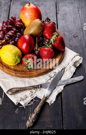 Verschiedene saftige reife Früchte. Erdbeere, Kiwi, Apfel, Birne, Banane, Trauben. Köstliche tropische Früchte auf einem hölzernen Hintergrund. Gesundes Frühstückskonzept Stockfoto