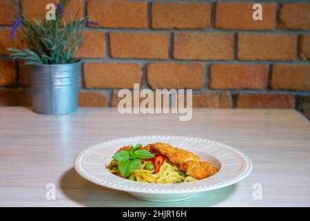 Spaghetti Green Curry mit knusprigem Huhn, Spaghetti mit grünem Curry-Huhn auf Holztisch Stockfoto