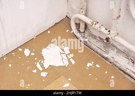 Das Innere ist ein altes Haus, das renoviert werden muss. Der zerbröckelnde weiße Putz von der Wand liegt auf dem Boden, in der Nähe des alten Heizkörpers. Stockfoto