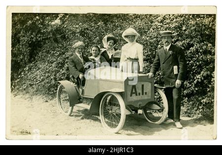 Originale amüsante Postkarte aus der Zeit des Edwardians mit glücklichen Touristen, Männern und Frauen, die Strohboote und Hüte tragen, in smarter sonntags bester Kleidung gekleidet sind, für ein Foto in einem Modellauto posten, fotografische (einige Charaktere) Requisiten, während eines Sommerurlaubs am Meer. Das Modellauto hat seltsamerweise die Buchstaben A.I. fotografiert von H. Batty, The Jetty Studio, Clacton-on-Sea, Essex, Großbritannien um 1910, 1912. Stockfoto