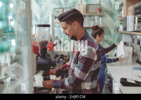 Porträt eines fokussierten männlichen Barista, der in der Nähe der Kaffeemühle im Café steht Stockfoto
