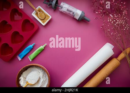 Backvorbereitung: Herzförmige Silikonform, Nudelholz, Süßwarenspritze, Glasur, Mehl, Zucker. Speicherplatz kopieren. Valentinstag-Konzept. Hochwertige Fotos Stockfoto