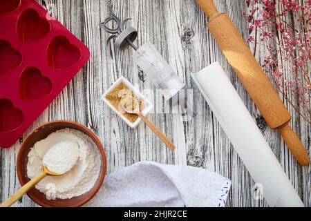 Backvorbereitung: Herzförmige Silikonform, Nudelholz, Süßwarenspritze, Glasur, Mehl, Zucker. Valentinstag-Konzept. Gypsophila-Dekoration. Hochwertige Fotos Stockfoto