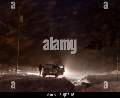 Menschen in einer verschneiten Nacht mit einem kaputten Auto auf der Straße Stockfoto