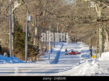 Mann, der Schnee von einem roten Pickup auf der Straße säubert Stockfoto