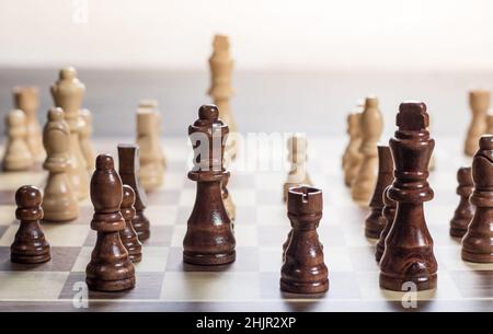 Schachbrett mit Schachspiel, das vor hellem Hintergrund gespielt wird. Schwarze Stücke im Vordergrund Stockfoto