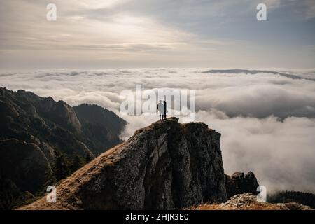 Junges Paar, das auf einem Felsen sitzt und den Blick über die Wolken genießt Stockfoto