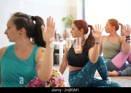 Detail von jungen gesunden Frauen, die Yoga mit Halbwirbelwirbelverdrehung praktizieren. Gruppe von kaukasischen Frauen, die Yoga in der Yogaklasse in Ardha Matiendrasana Haltung machen. Stockfoto