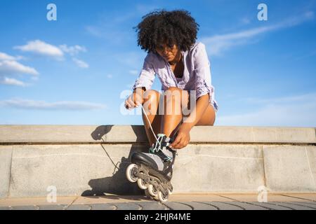 Schöne junge schwarze Frau, die Inline-Skates anzieht Stockfoto