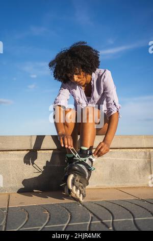 Schöne junge schwarze Frau, die Inline-Skates anzieht Stockfoto